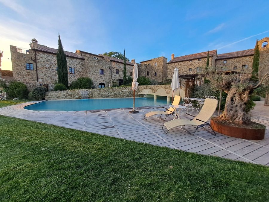 Pool mit Holzdeck vor den Natursteinhäusern von Castel Brunello im Abendlicht