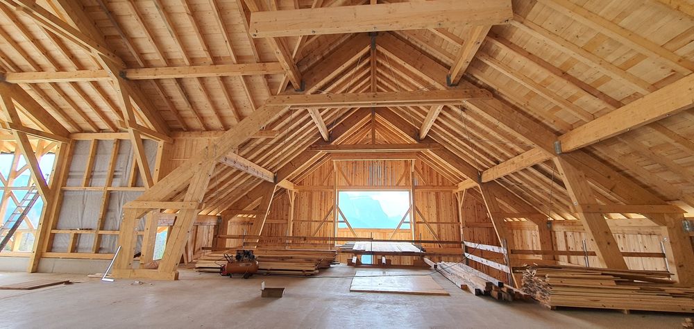 Offener Holzdachstuhl während der Bauphase mit Blick durch das Giebelfenster auf die Berge