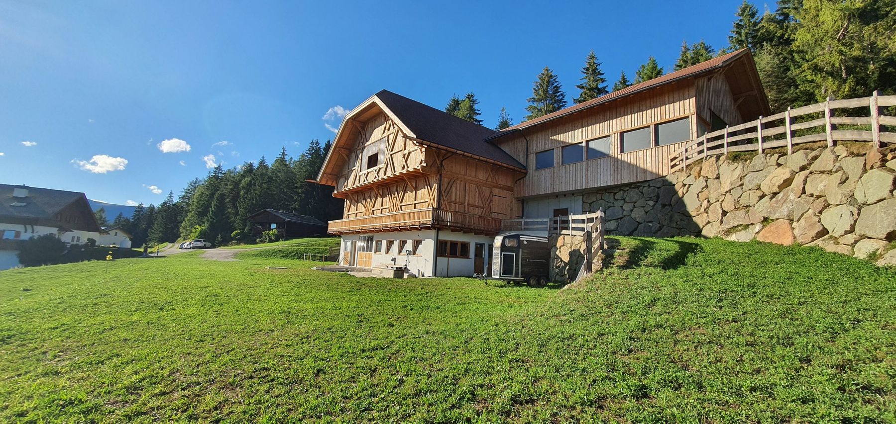 Gesamtansicht des neuen Wirtschaftsgebäudes in Lajen mit Holzfassade, Anbau und Steinmauer am Waldrand