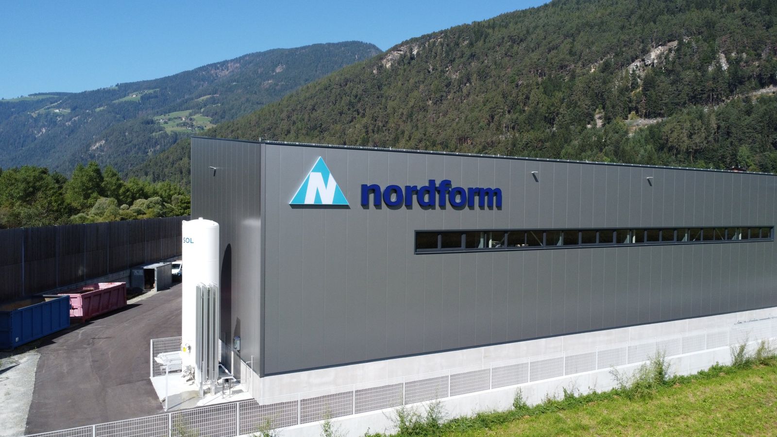 Neue Werkshalle Nordform mit dunkler Fassade und Fensterband vor bewaldetem Berghang
