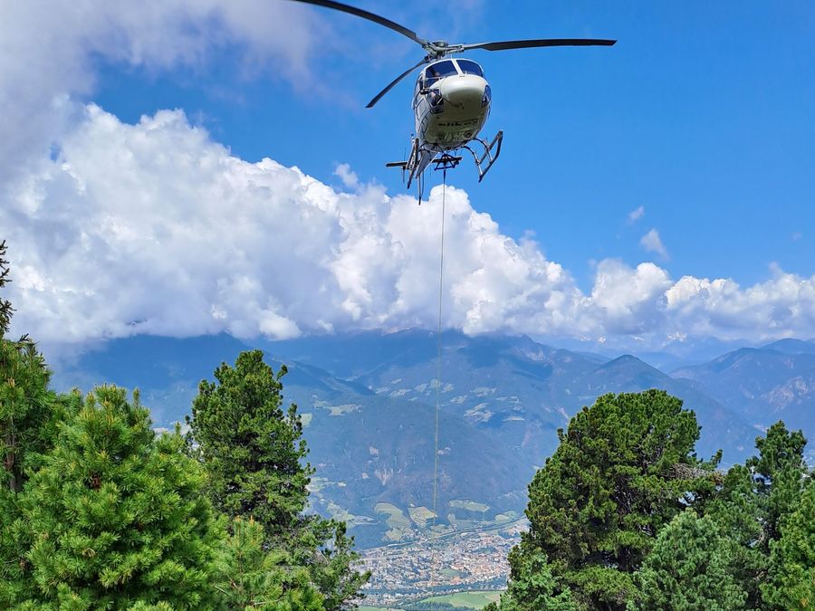 Hubschrauber fliegt Beton zu einer Baustelle im Wald an der Plose